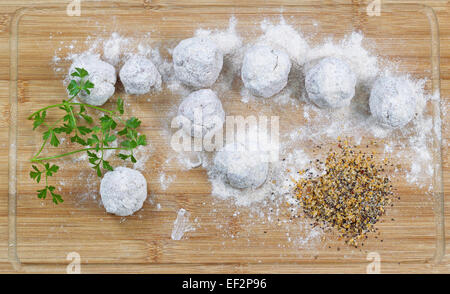 Uncooked floured homemade meatballs with parsley and spices on natural bamboo board. Top view angled shot. Stock Photo