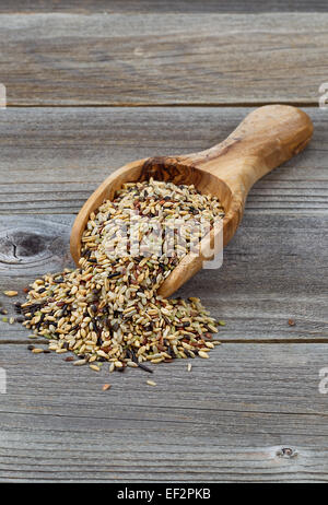 Vertical orientation of a wooden scoop filled with whole grain rice spilling onto rustic wood Stock Photo
