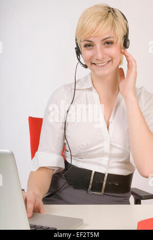 Blond woman wearing headset while working on laptop Stock Photo