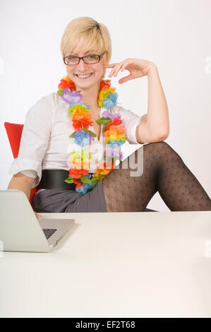Blond woman sitting at desk wearing a lei Stock Photo