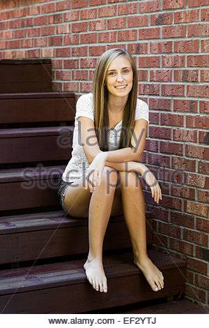 Happy tanned Caucasian teenager girl seated on a wooden dock in a Stock ...