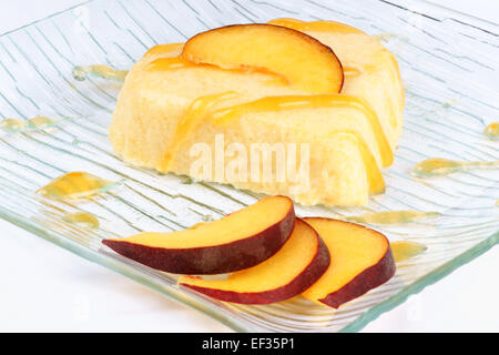 Heart shaped peach bavarian cream dessert (bavarese) with peach sauce and peach slices on a transparent glass plate. Stock Photo