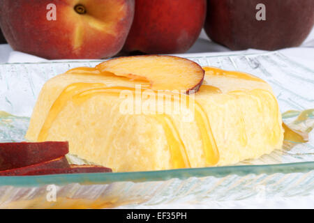Heart shaped peach bavarian cream dessert (bavarese) with peach sauce and peach slices on a transparent glass plate. Stock Photo