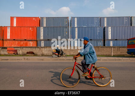 A man is riding bicycle on R.E. Martadinata Street, in a background of Port of Jakarta container terminal in Tanjung Priok, Jakarta, Indonesia. Stock Photo