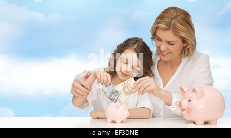 mother and daughter putting money to piggy banks Stock Photo