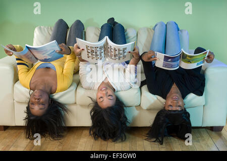 Three friends lying upside down on couch and reading Stock Photo