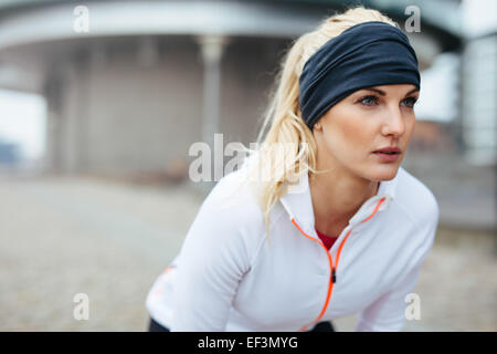 Portrait of young female athlete leaning over and looking away. Motivated and focused sporty woman before a run. Stock Photo