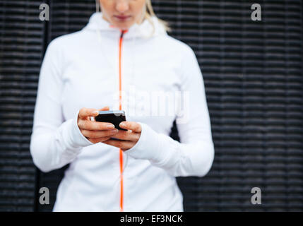 Cropped image of woman in sportswear using mobile phone. Focus on hands and smart phone. Stock Photo