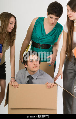 Three woman looking at a man crouched in a box Stock Photo