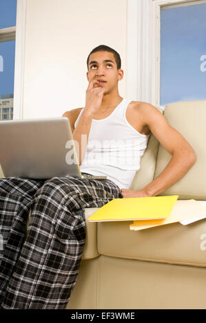 Pensive man sitting on couch with laptop Stock Photo