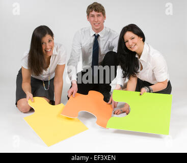 Three people sitting on floor looking at puzzle pieces Stock Photo