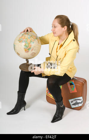 Woman sitting on suitcase while looking at globe Stock Photo