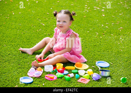 Toddler kid girl playing with food toys sitting in green turf grass garden Stock Photo