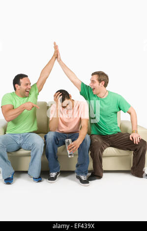 Two men giving high five while another man holds his head Stock Photo