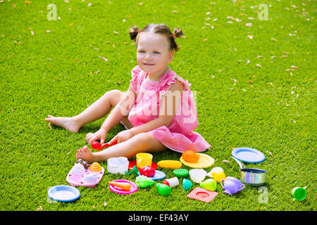 Toddler kid girl playing with food toys sitting in green turf grass garden Stock Photo