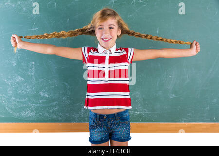 Braided student blond girl playing in green chalkboard with braids at school classroom Stock Photo