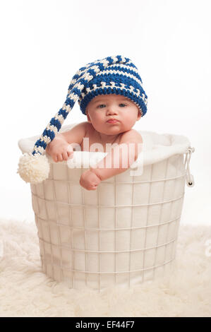 A 4 month old baby boy wearing a stocking cap. He is sitting in a wire basket with clenched fists and a pouting expression. Shot Stock Photo