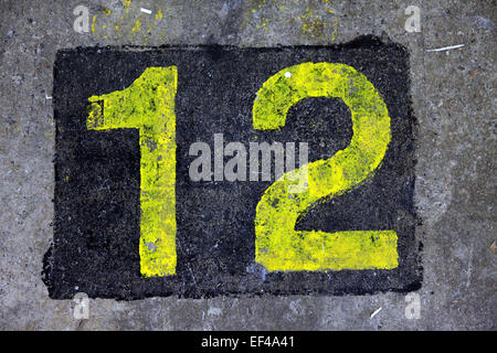Top view of the number 12 painted in a stencil style in yellow color on the ground. It's in a black square Stock Photo