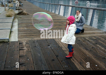 Little girl looking in wonder at a huge soap bubble while her mother looks on, Vancouver, BC, Canada Stock Photo
