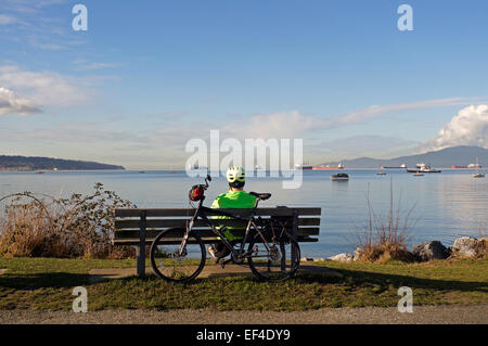 Male cyclist sitting on a park bench overlooking English Bay, Vanier Park, Vancouver, BC, Canada Stock Photo