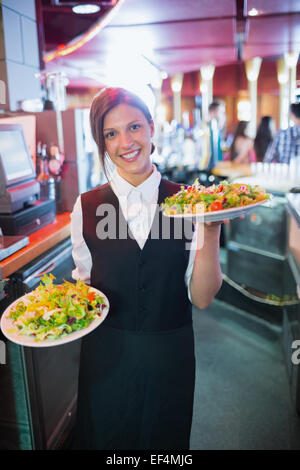 Pretty barmaid holding plates of salads Stock Photo