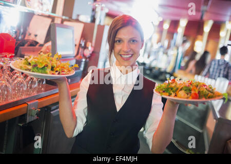 Pretty barmaid holding plates of salads Stock Photo