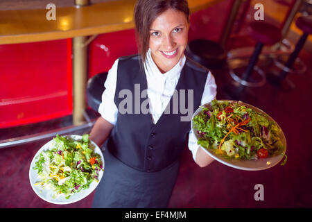 Pretty barmaid holding plates of salads Stock Photo