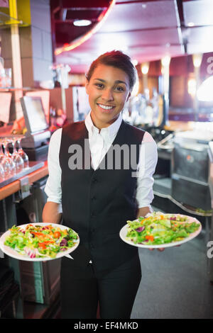 Pretty barmaid holding plates of salads Stock Photo