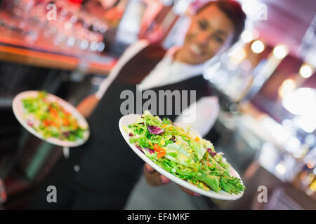 Pretty barmaid holding plates of salads Stock Photo