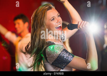 Happy blonde singing karaoke into mic Stock Photo