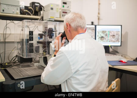 Biochemist using large microscope and computer Stock Photo