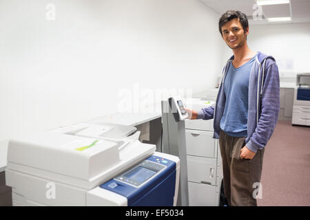 Smiling student standing next to the photocopier Stock Photo