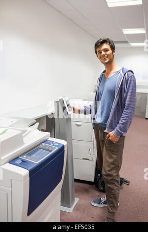 Smiling student standing next to the photocopier Stock Photo