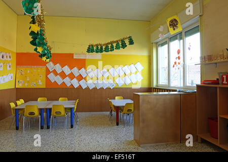 Preschool classroom with yellow chairs and table with drawings of children hanging on the walls Stock Photo