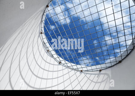 Abstract white interior fragment. Blue cloudy sky behind the round window with metal grid Stock Photo