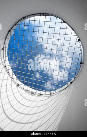 Abstract empty white interior fragment. Blue cloudy sky behind the round window with metal grid Stock Photo