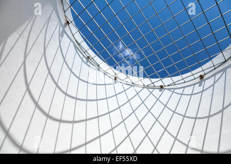 Abstract white interior fragment. Blue sky behind the round window with metal grid Stock Photo