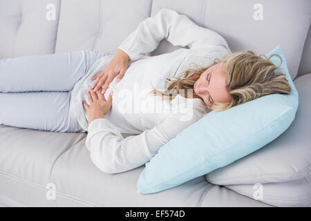 Blonde lying on couch getting stomach pain Stock Photo