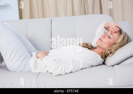 Blonde lying on couch getting stomach and head ache Stock Photo