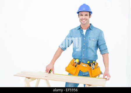 Happy male carpenter measuring wooden plank Stock Photo
