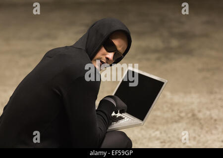 Hacker in hooded jumper using laptop Stock Photo