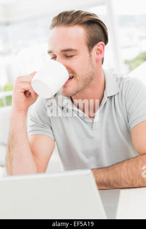 Cheerful businessman using laptop while drinking Stock Photo