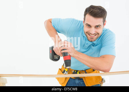 Smiling construction worker using hand drill on wooden plank Stock Photo