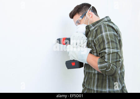 Carpenter using drill machine on white wall Stock Photo