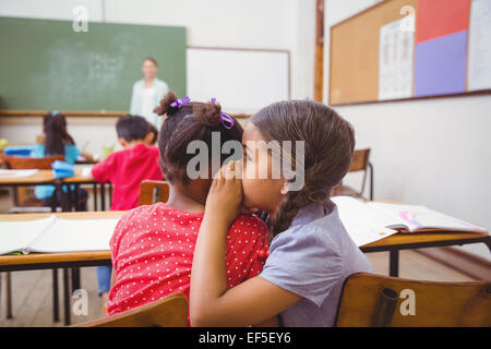 Cute pupils whispering in classroom Stock Photo