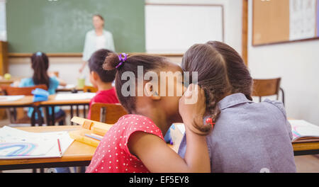 Cute pupils whispering in classroom Stock Photo