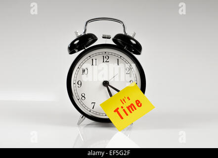 Alarm clock with a yellow note saying it's time Stock Photo