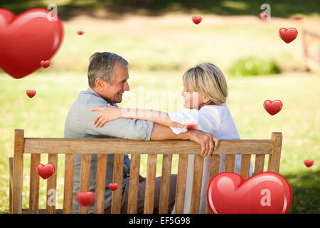 Composite image of happy retired couple sitting on the bench Stock Photo