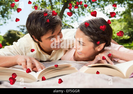 Composite image of two friends looking at each other while reading books on a blanket Stock Photo