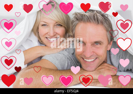 Composite image of couple smiling under the covers Stock Photo